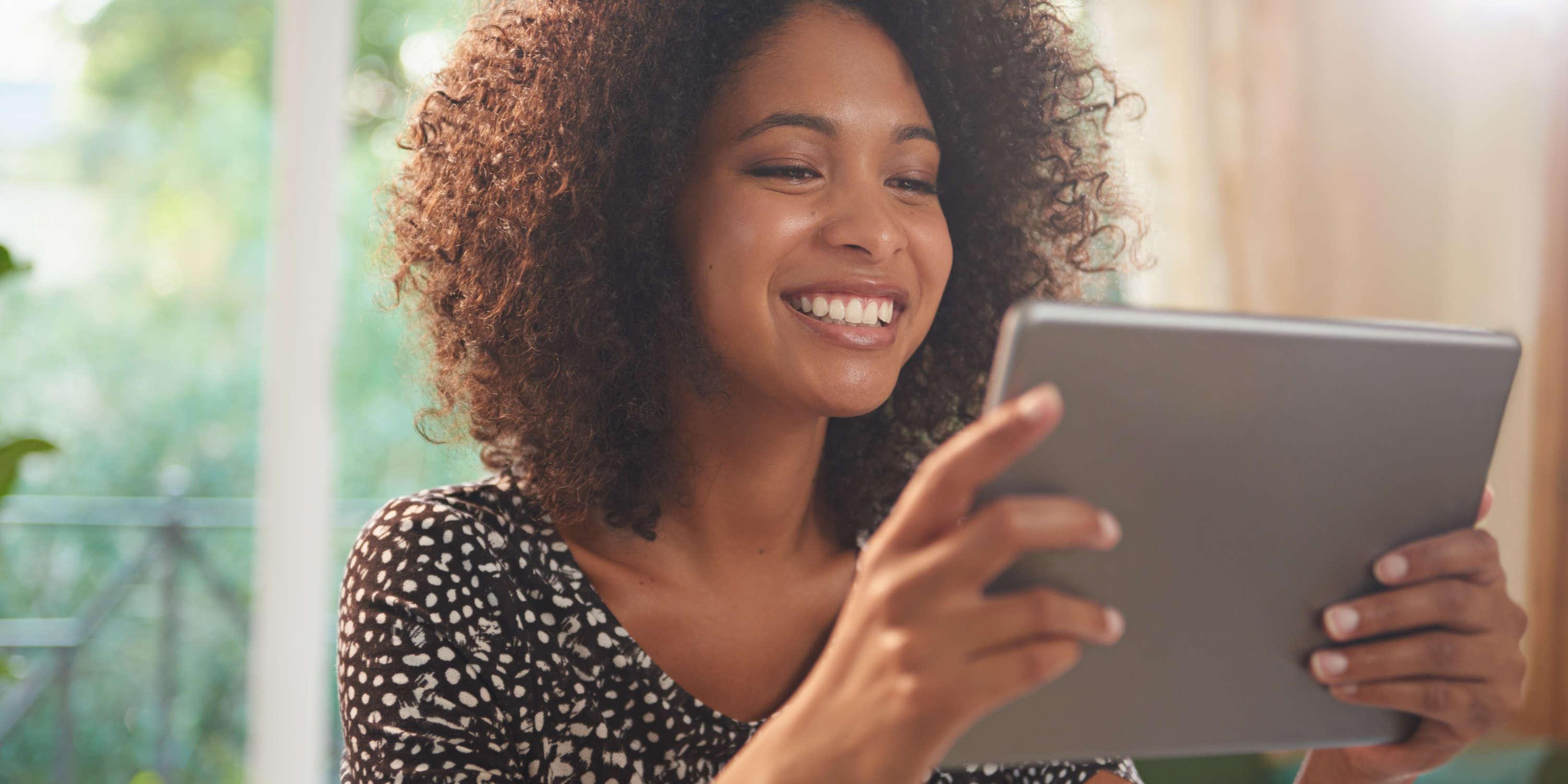 A black woman smiling while looking at a tablet.