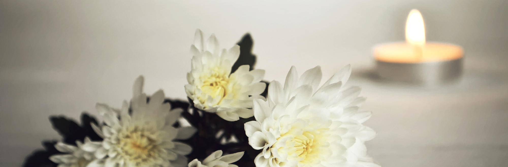 Close up on a bouquet of white flowers laying on its side, a single tea light candle lit in the background.