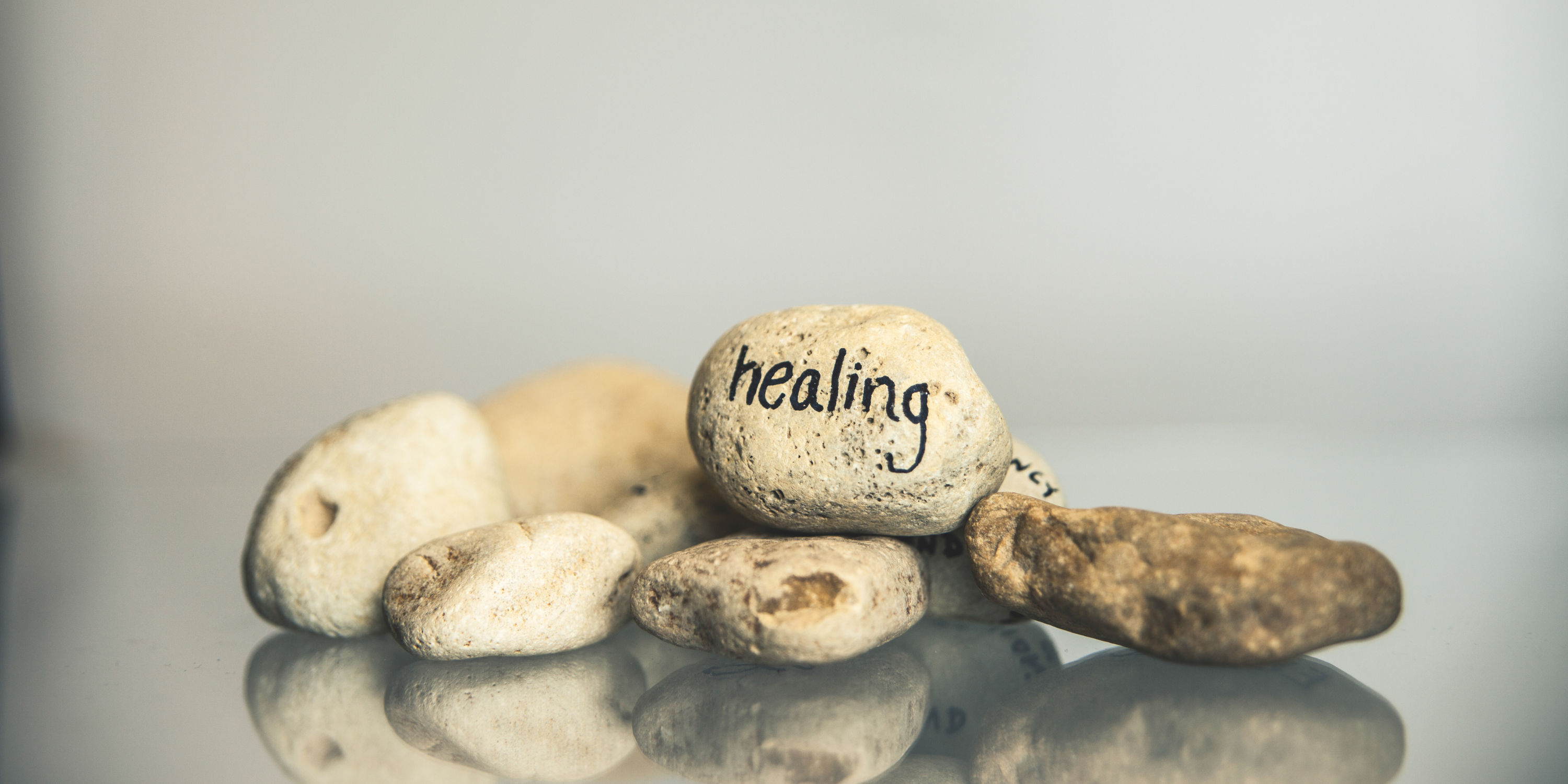 Small rocks resting on a table, with one rock reading "healing" in black ink.