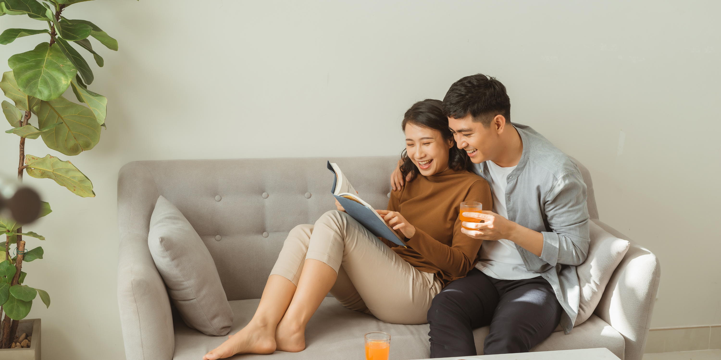 Couple sitting together on couch, both interested in reading a book.