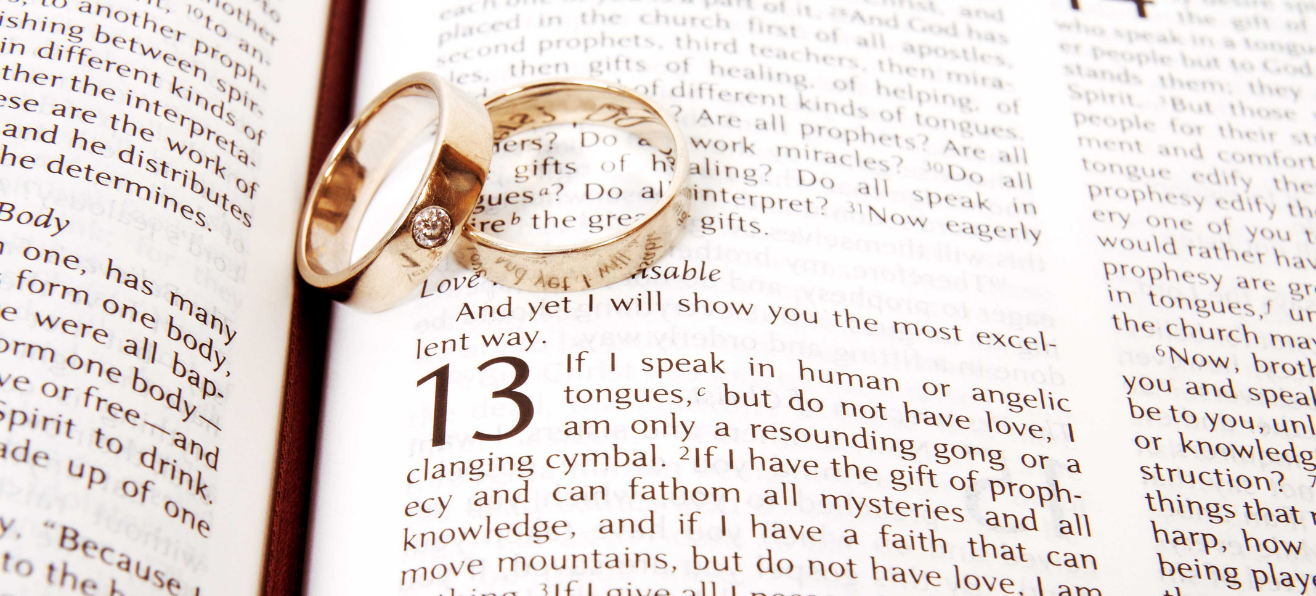 Two wedding bands resting on an open Bible, on 1 Corinthians 13.