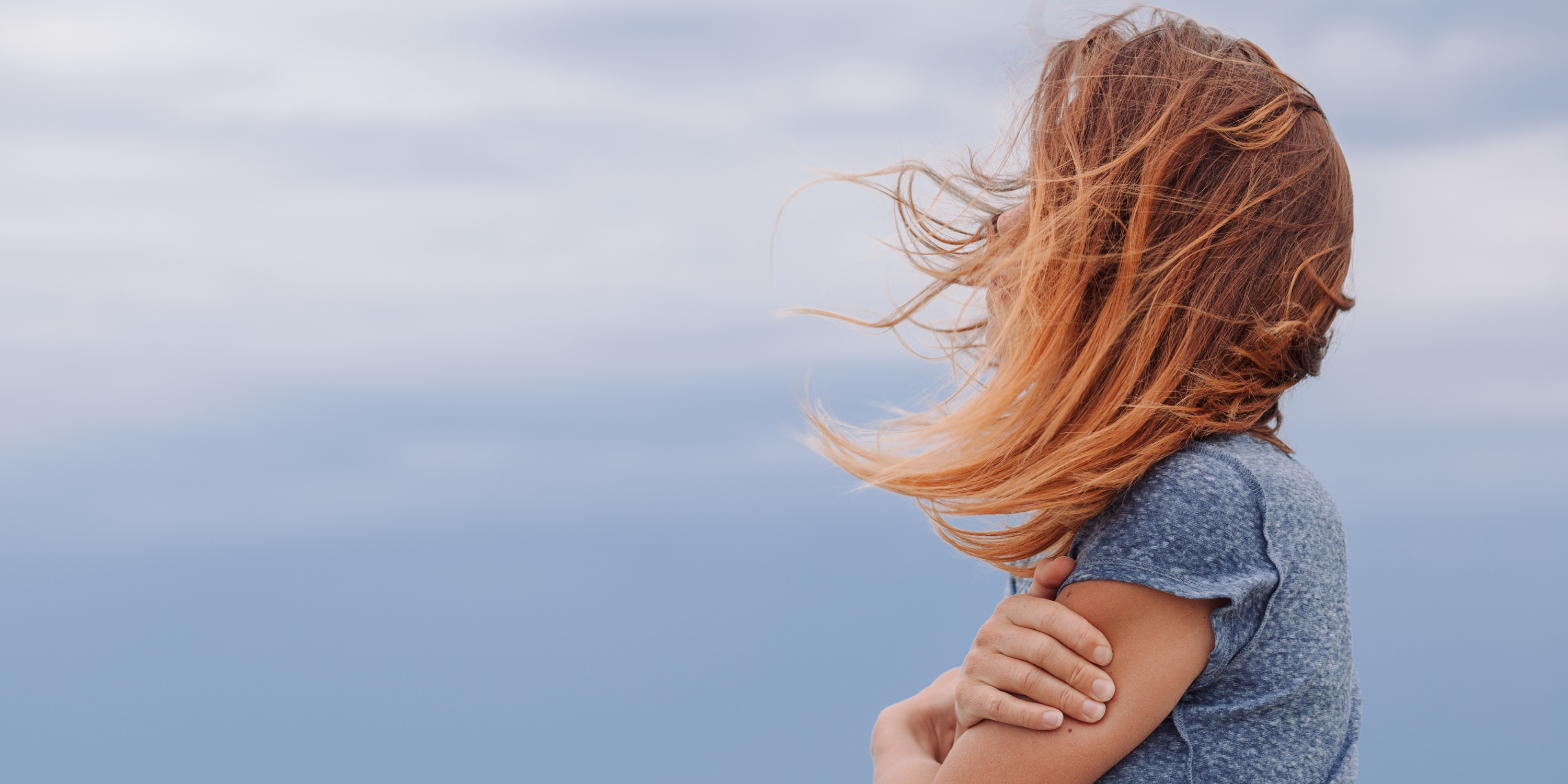 Woman looking out at the sea, wind blowing her hair
