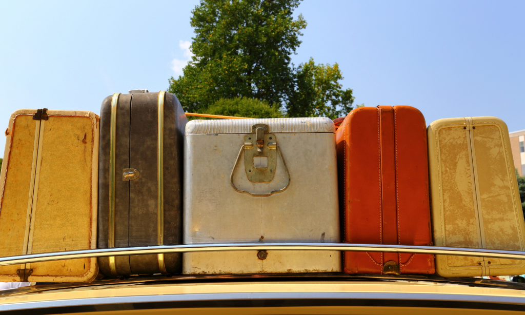 A set of five vintage-looking suitcases and luggage sitting on top of the roof of a car.