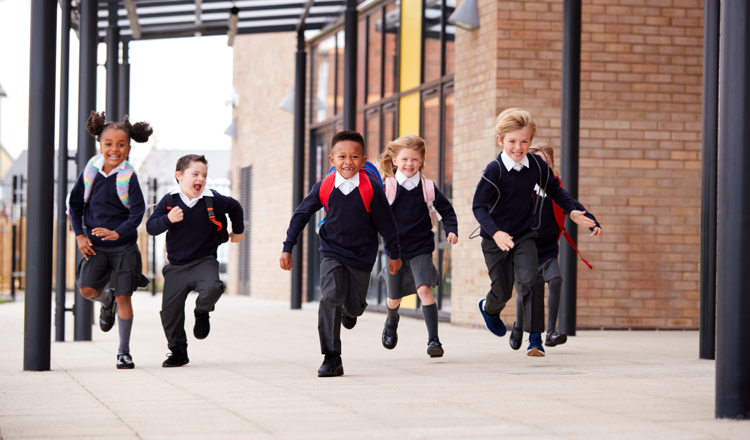 A group of diverse elementary students running excitedly through a school hallway, smiles on their faces.