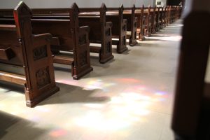 A row of pews within the Basilica of Our Lady Immaculate Parish, with reflections of stained glass on the floor.