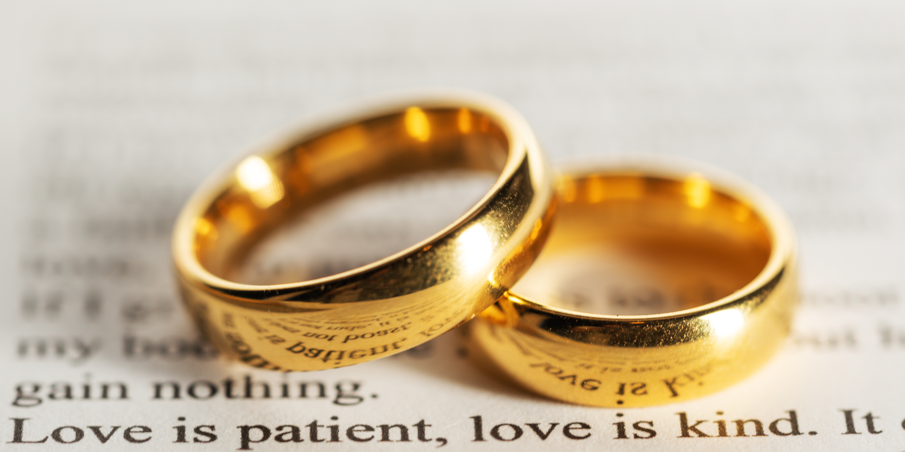 Wedding rings sitting on top of a Bible passage that reads Love is patient, love is kind.
