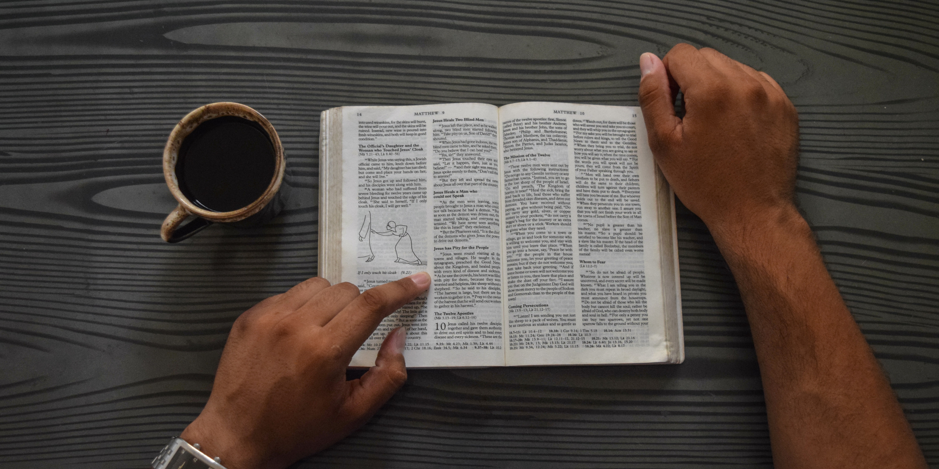 Top view of a person reading a Bible, with a cup of coffee next to them on the table