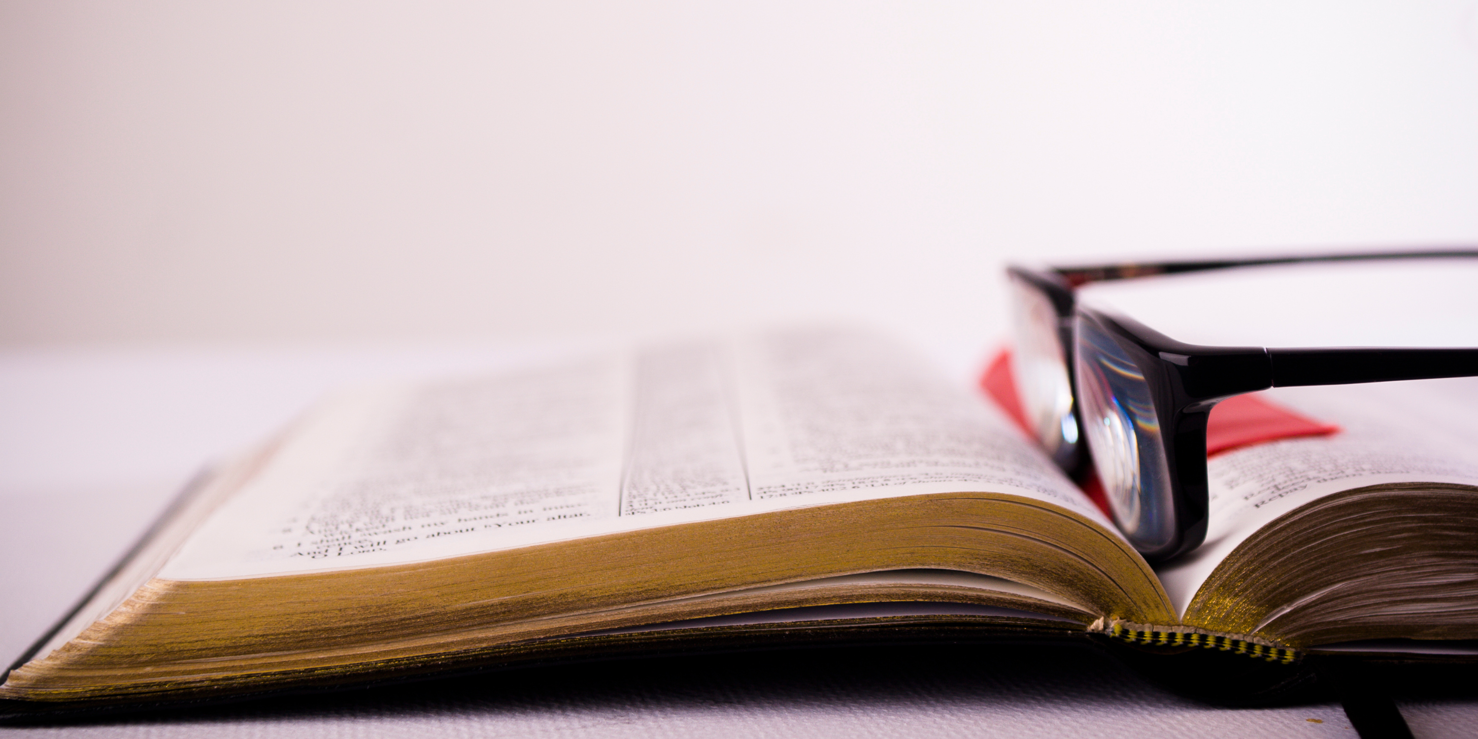A pair of black glasses rests atop a Bible.