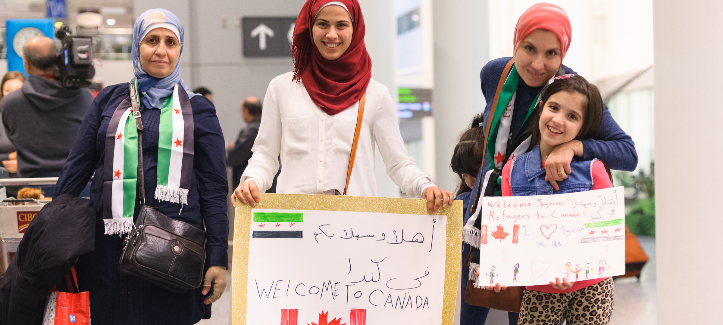 A group of women and a younger girl at the airport, holding welcome signs.
