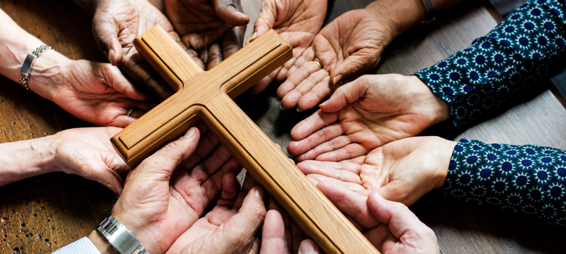 A variety of hands holding onto a wooden cross.